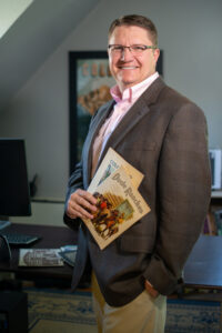 Jerry Frank poses in his office in Read Hall holding literature about dude ranches of the Old West.