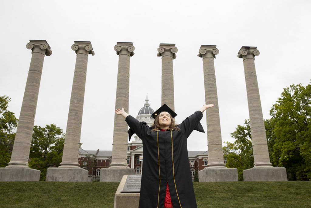 Enthusiastic graduate Sarah Sabatke raises her arms in front of MU's Columns