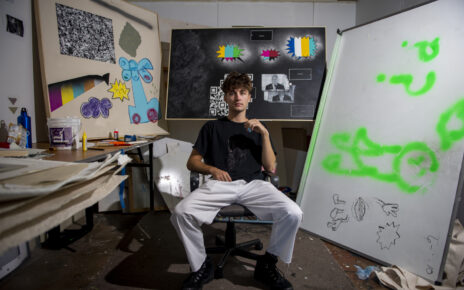 Zach Johnson sits in front of his artwork in his MU studio.